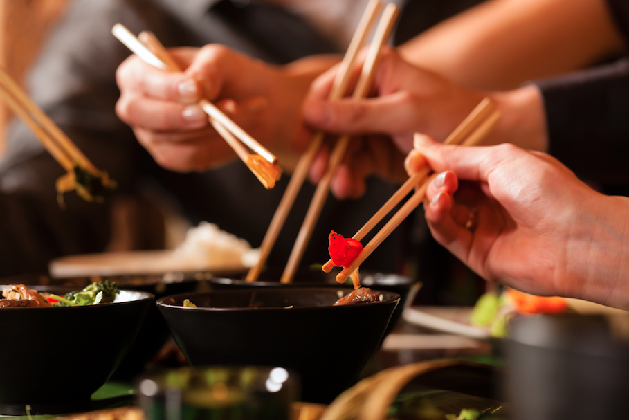 Hands with chopsticks eating Asian food from bowls