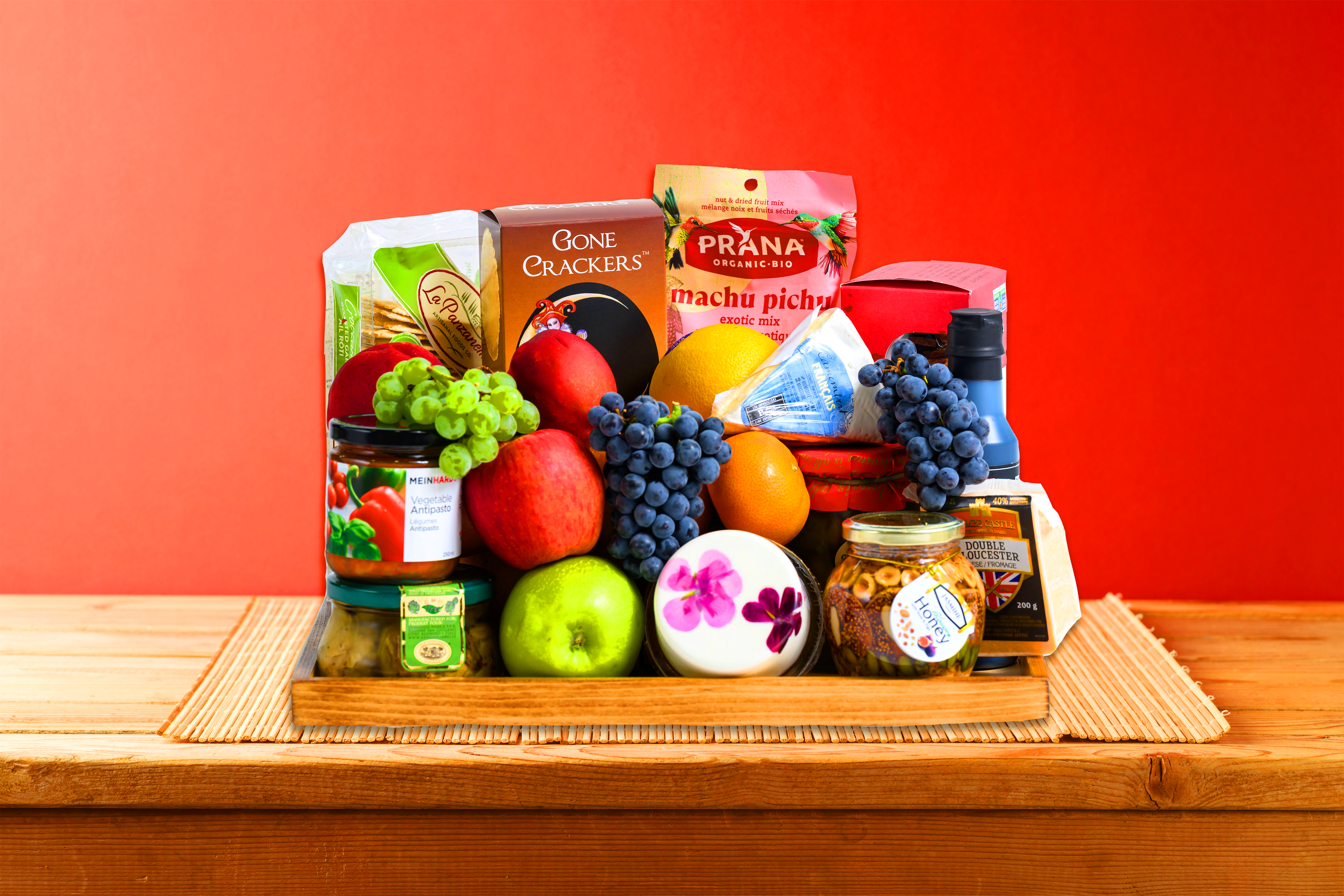 gift basket featuring fine cheeses, savory snacks, and fresh seasonal fruit on wooden charcuterie board.