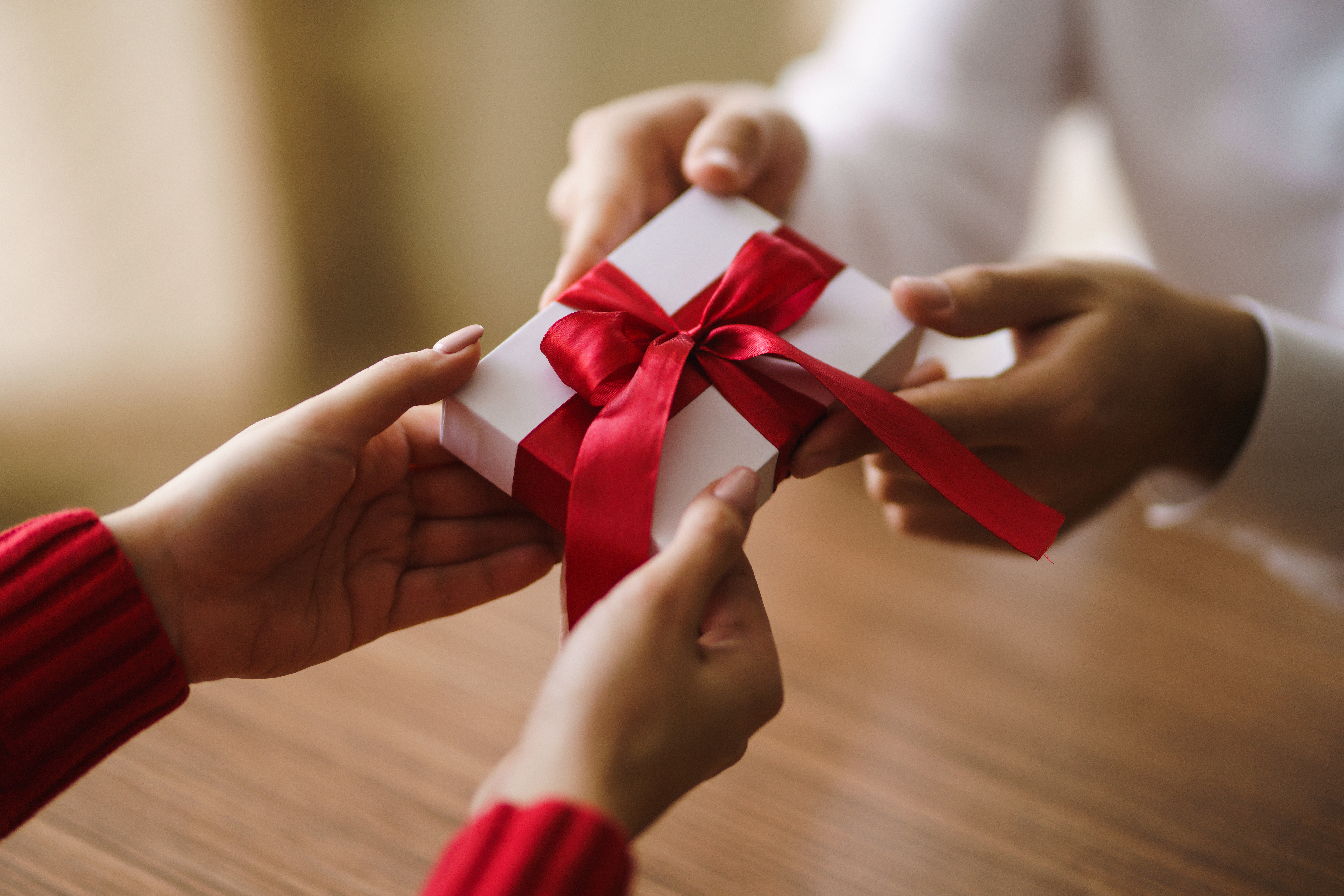 Man gives to his woman a gift box with red ribbon. Hands of man gives surprise gift box for girl. Young loving couple celebrating Valentine's Day. Relationship, surprise, Birthday concept